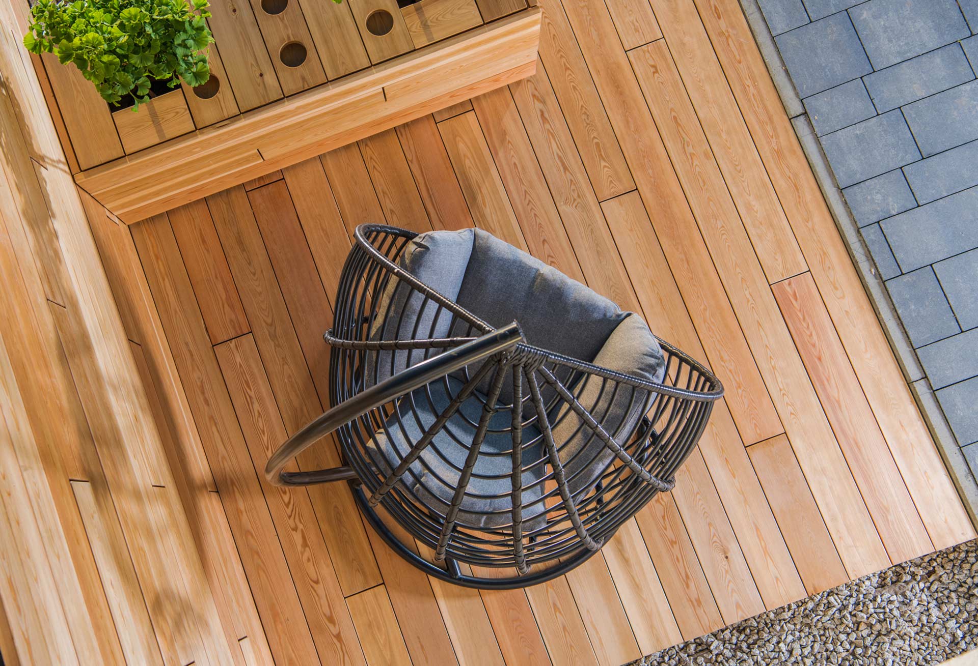 Holzterrasse mit hellbraunen Dielen und dunklem Gartenstuhl aus der Vogelperspektive