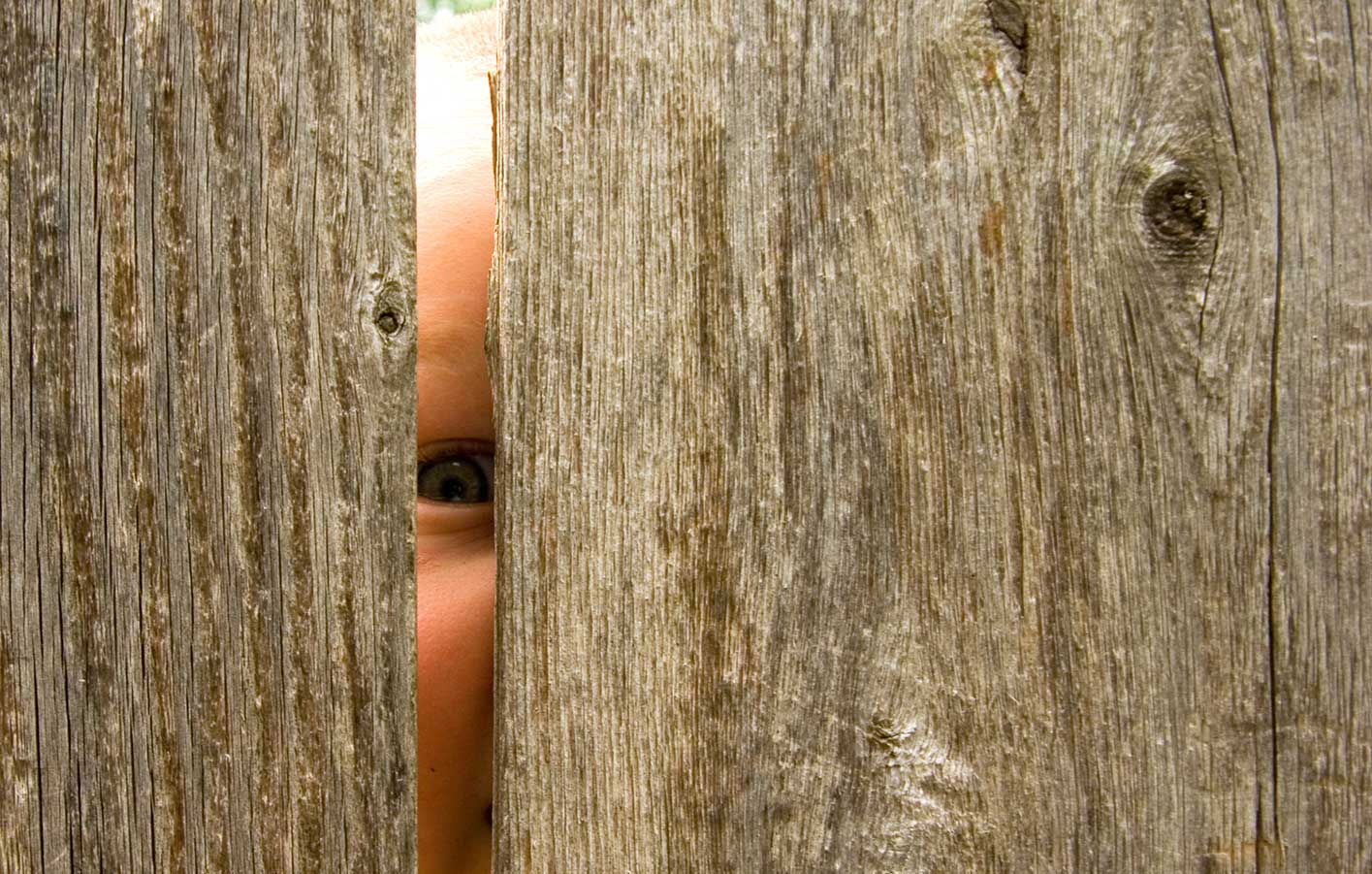 Neugieriges Kind schaut durch einen Sischutzzaun aus Holz